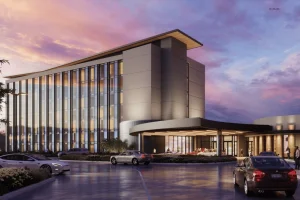 Penn Entertainment sets June opening for Hollywood Casino Columbus hotel debut. Modern multi-story hotel tower at Hollywood Casino Columbus with glass façade, covered entrance, and cars arriving at dusk under a colorful sunset sky.